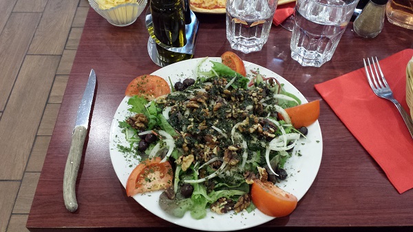 Salad in a restaurant (greens, tomatoes, onions, toasted walnuts)
